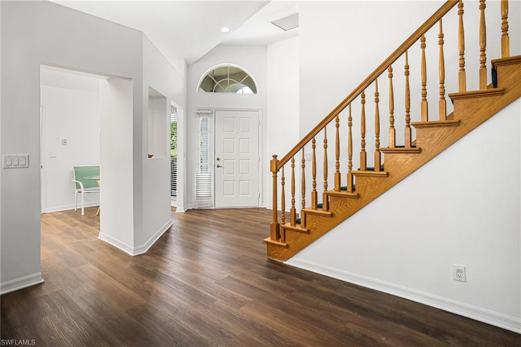Entryway featuring wood-finish flooring, a white paneled front door, an arched transom window, and a wooden staircase with balusters