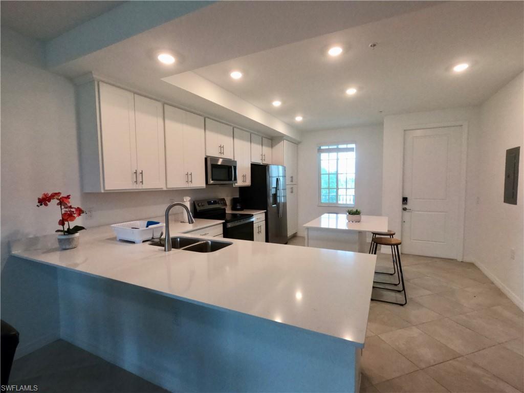 Kitchen with white cabinets, a peninsula, stainless steel appliances, recessed lighting, and a kitchen bar