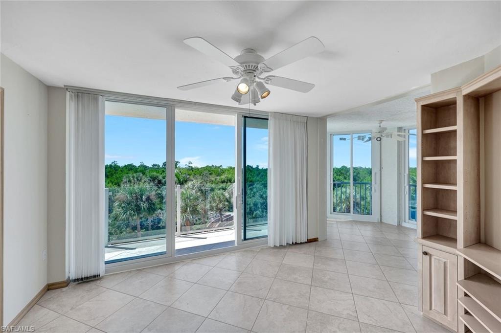 Unfurnished room with partial Gulf view,  light tile patterned floors, a wall of windows, and a ceiling fan