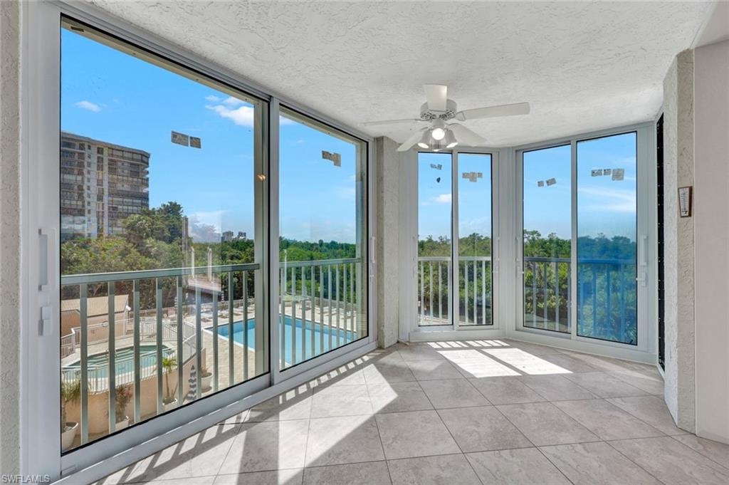 Unfurnished sunroom with expansive windows, tile patterned flooring, healthy amount of natural light, a textured ceiling, and view of scattered trees