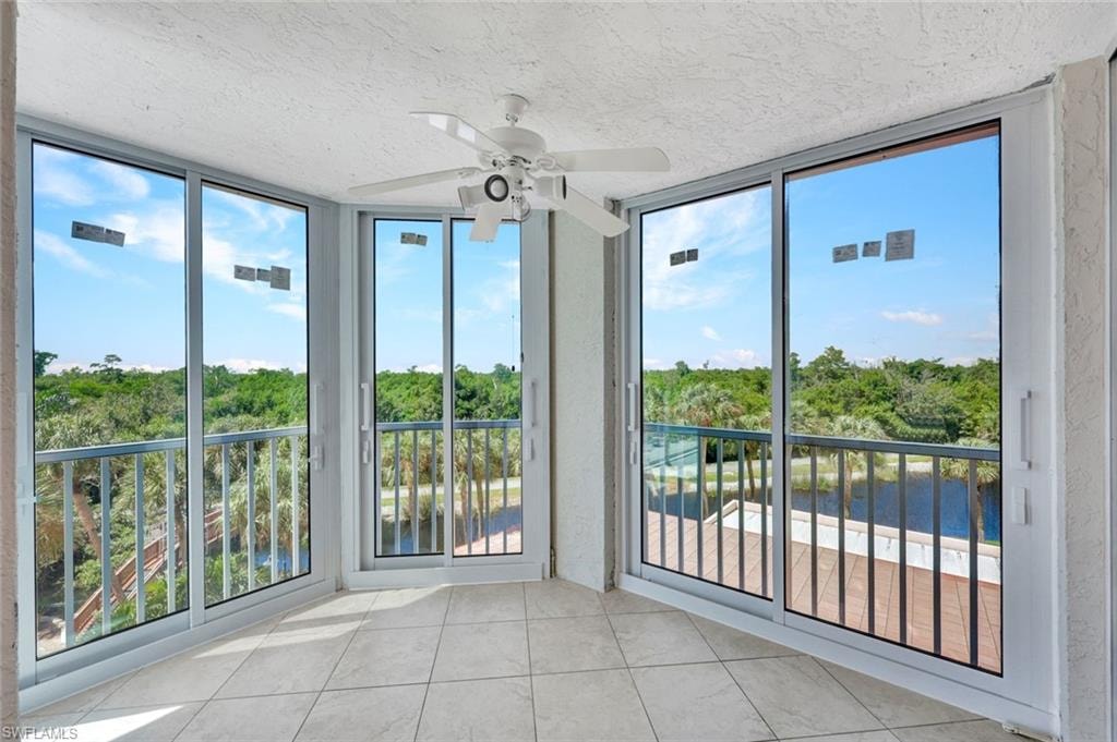 Unfurnished sunroom featuring view of scattered trees, tile patterned floors, a textured ceiling, and a wall of windows