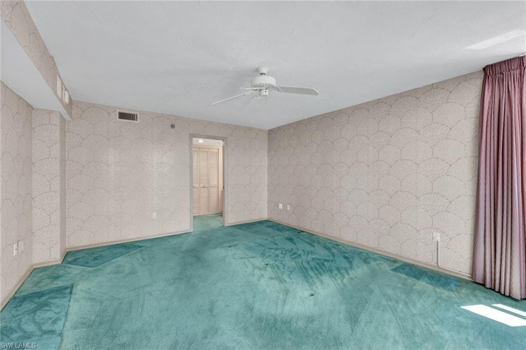 Carpeted primary bedroom with wallpapered walls and ceiling fan