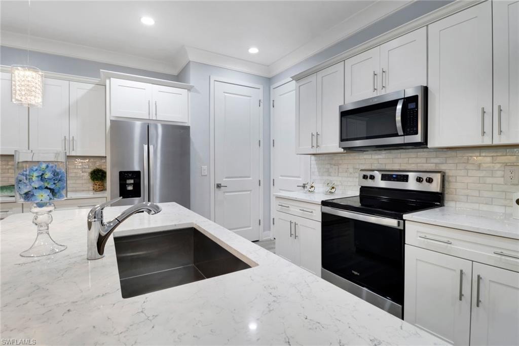 Kitchen with tasteful backsplash, appliances with stainless steel finishes, ornamental molding, pendant lighting, and white cabinetry