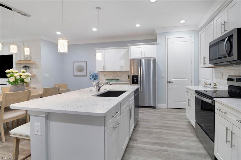 Kitchen featuring stainless steel appliances, an island with sink, white cabinets, light stone countertops, and hanging light fixtures