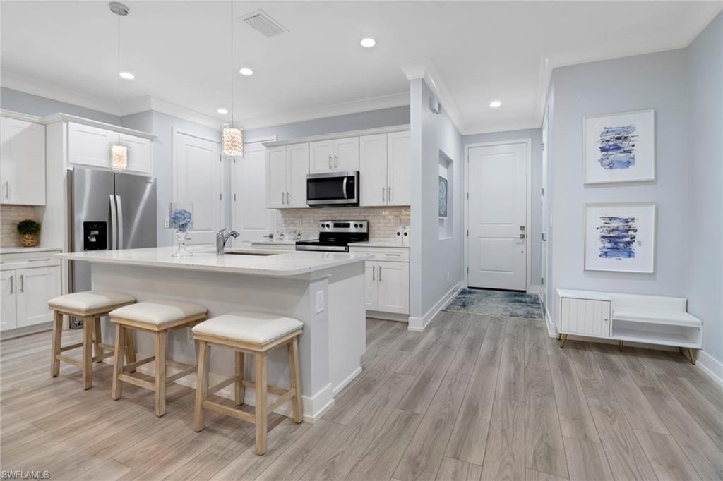 Kitchen with hanging light fixtures, stainless steel appliances, white cabinetry, a kitchen breakfast bar, and a kitchen island with sink
