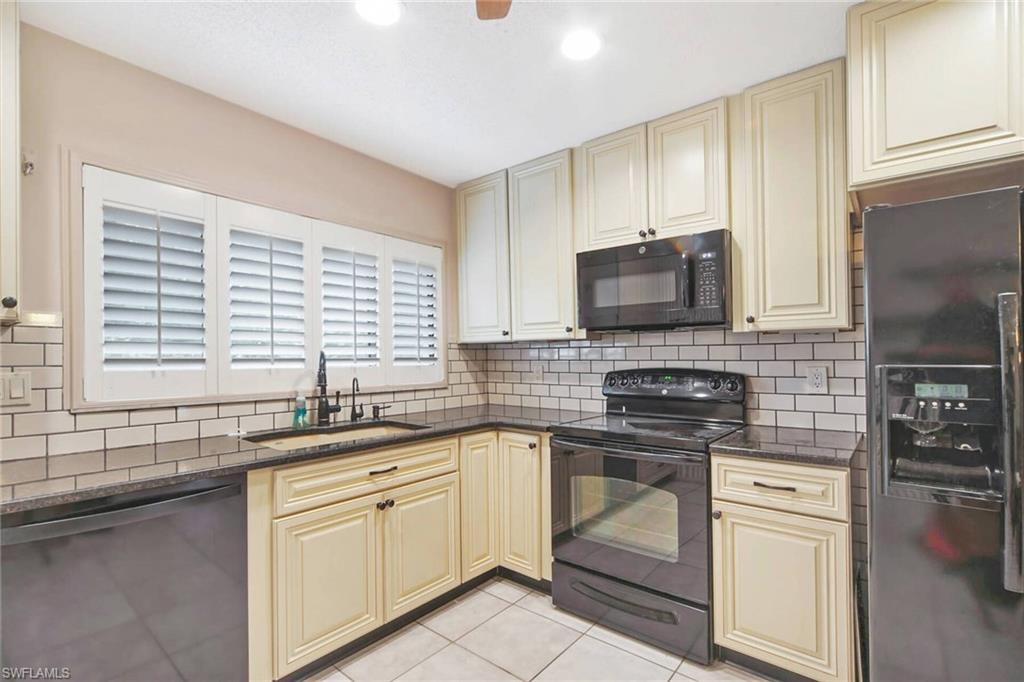 Kitchen boasts dovetail cabinetry black appliance package plantation shutters and synthetic granite double sinks