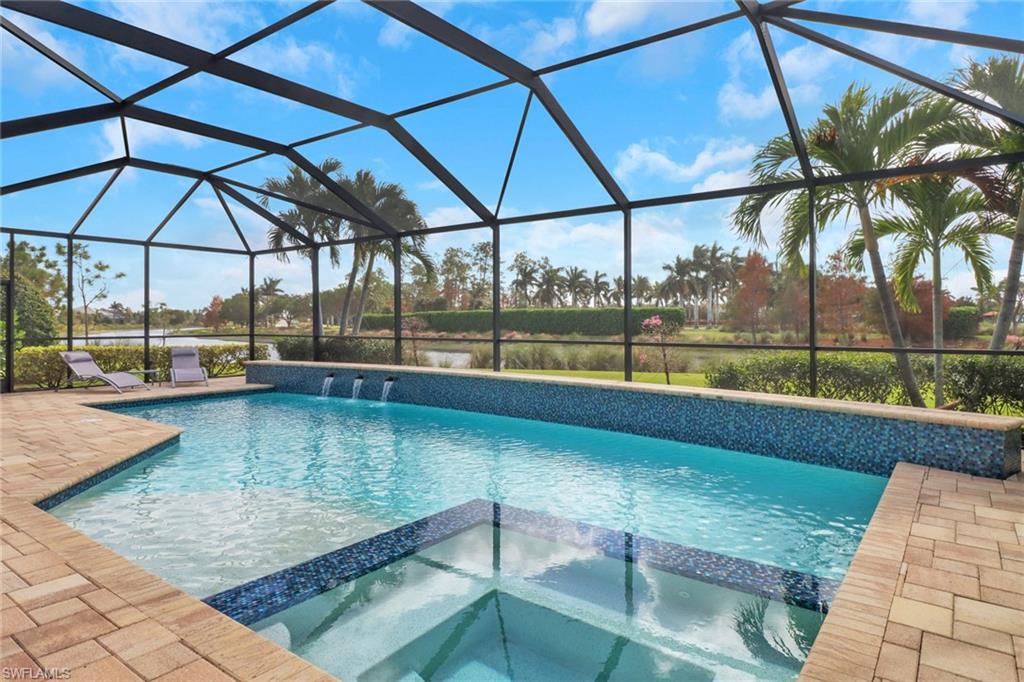 View of swimming pool featuring an in ground hot tub, pool water feature, a patio, and glass enclosure