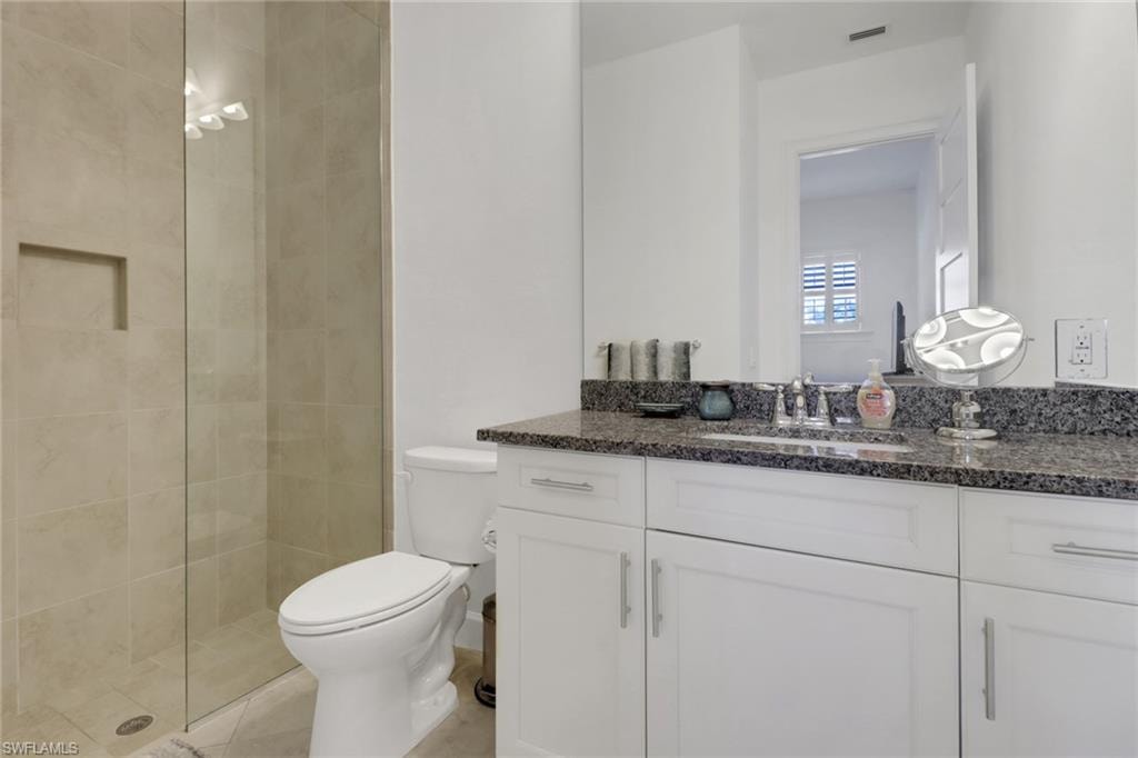 Bathroom featuring toilet, vanity, a tile shower, and tile patterned floors