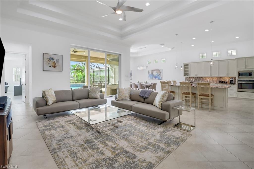 Tiled living room with a high ceiling, ceiling fan, and a raised ceiling