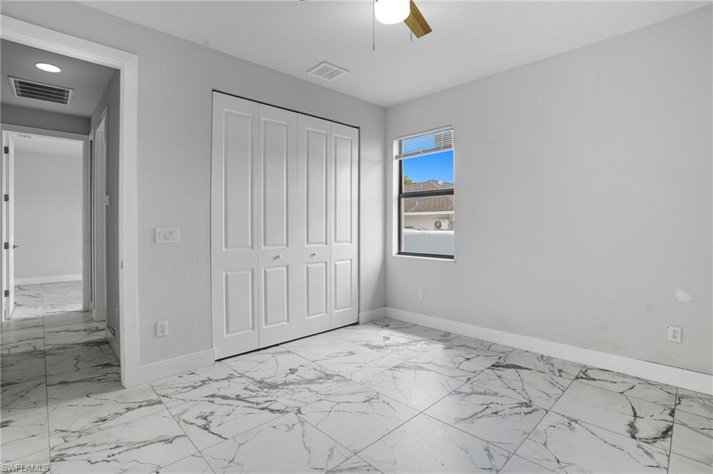 Unfurnished bedroom with light marble finish floors, a closet, and a ceiling fan