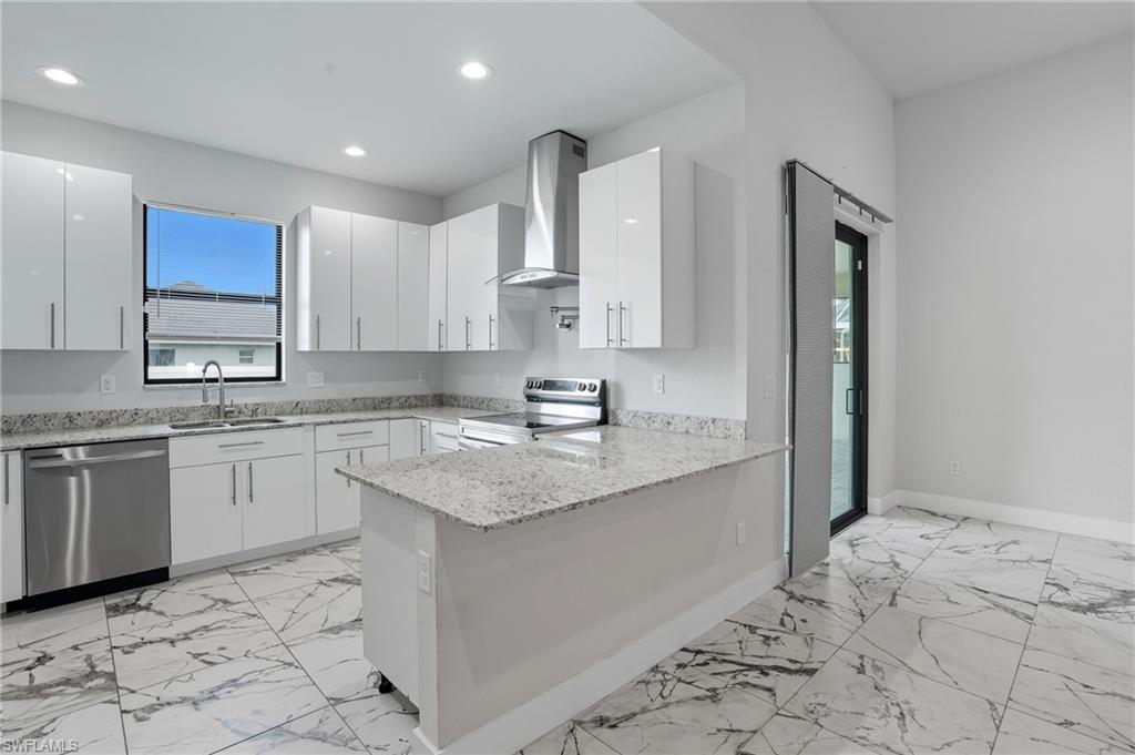 Kitchen with light stone countertops, stainless steel appliances, wall chimney range hood, a peninsula, and white cabinets