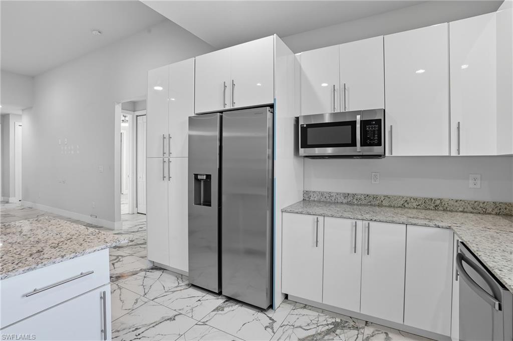 Kitchen with stainless steel appliances, light marble finish floors, white cabinets, and light stone counters