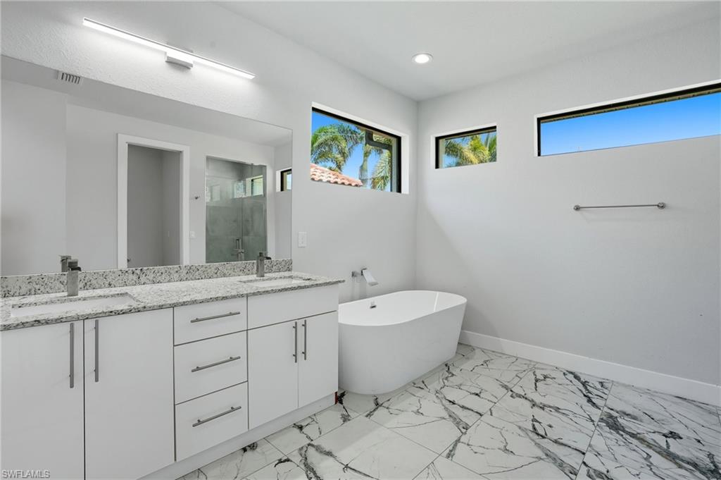 Bathroom with double vanity, a stall shower, a soaking tub, light marble finish flooring, and recessed lighting
