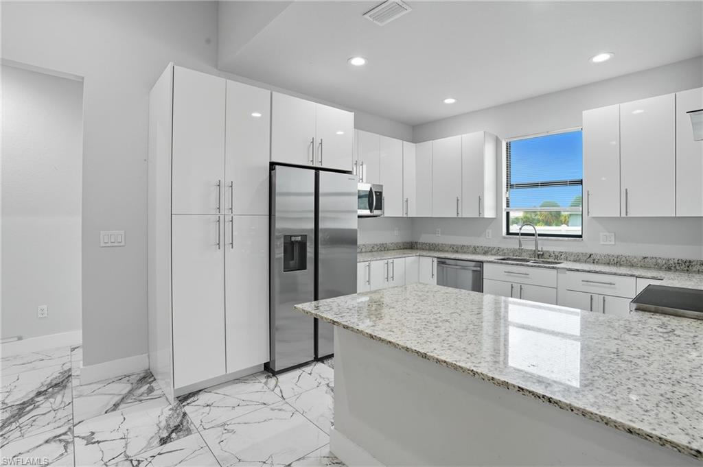 Kitchen featuring appliances with stainless steel finishes, light stone counters, white cabinets, light marble finish floors, and recessed lighting