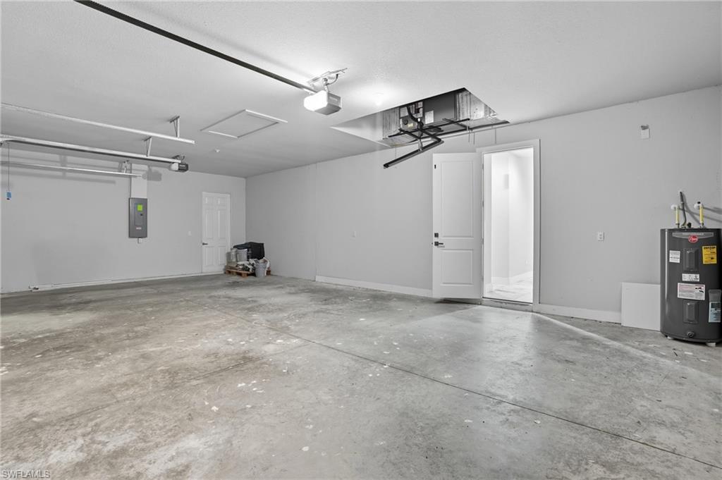 Garage with electric water heater, electric panel, and a garage door opener