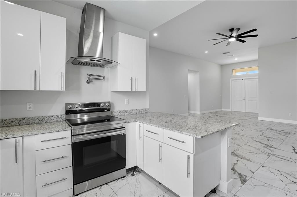 Kitchen with light marble finish floors, stainless steel range with electric cooktop, wall chimney range hood, white cabinets, and recessed lighting