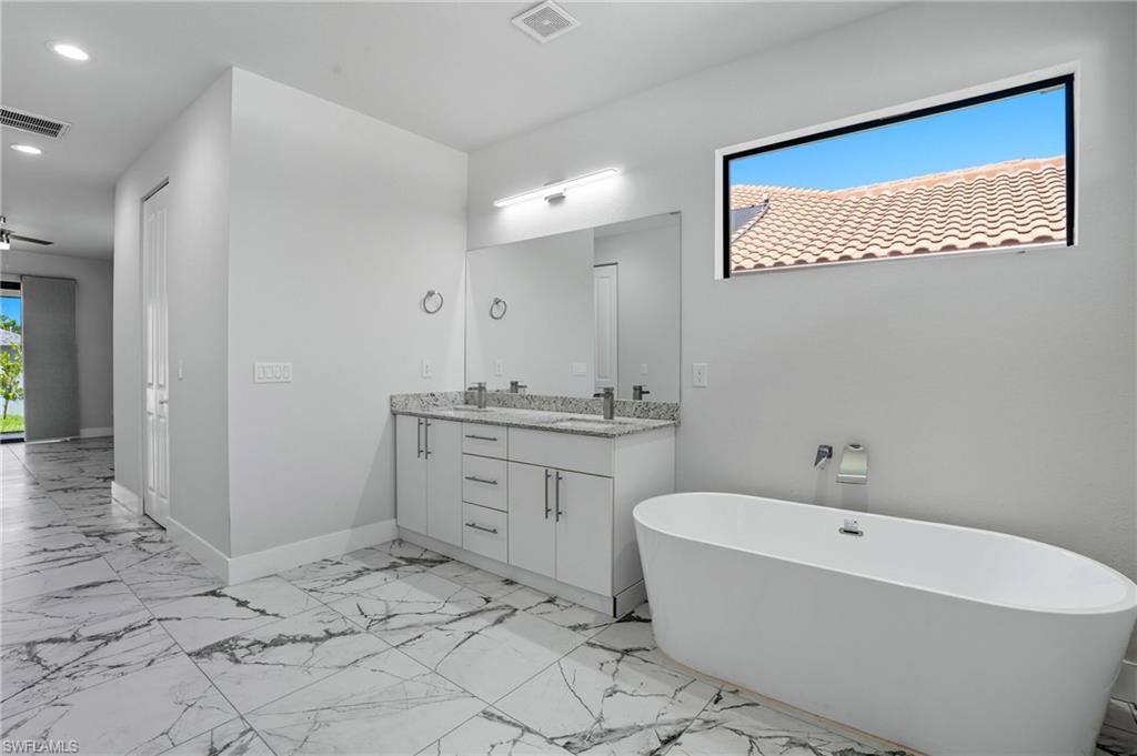 Full bathroom featuring double vanity, a freestanding tub, light marble finish flooring, recessed lighting, and a ceiling fan