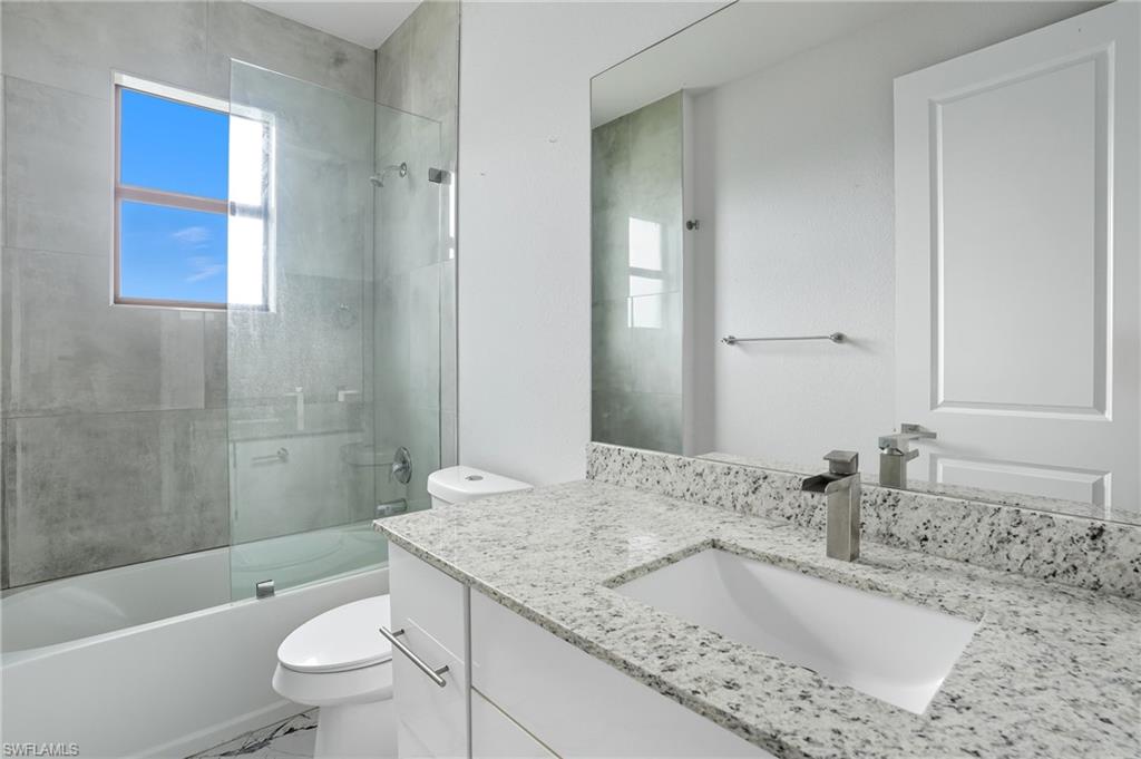 Bathroom with vanity, shower / bath combination with glass door, and healthy amount of natural light