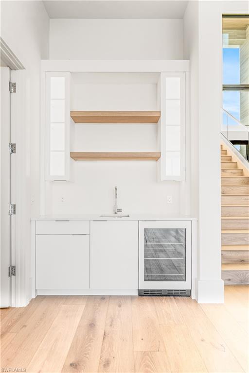 Indoor wet bar with white cabinetry, wine cooler, light wood-style floors, open shelves, and modern cabinets