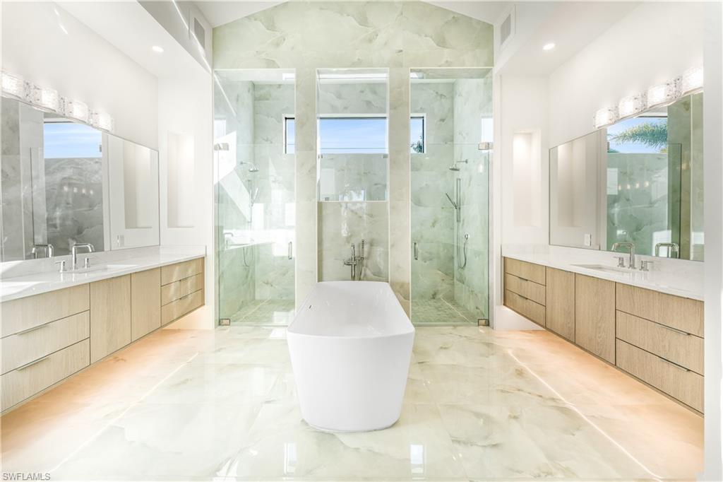 Bathroom with light marble finish floors, a marble finish shower, a soaking tub, and two vanities