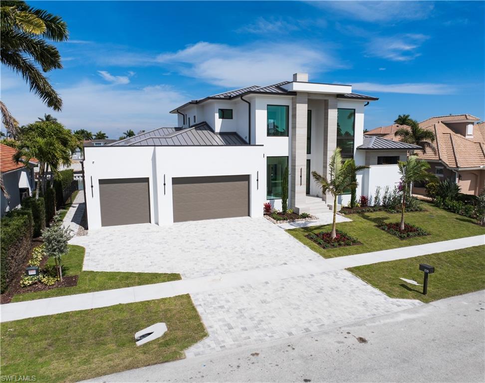 Contemporary home featuring a standing seam roof, a garage, a front yard, decorative driveway, and stucco siding