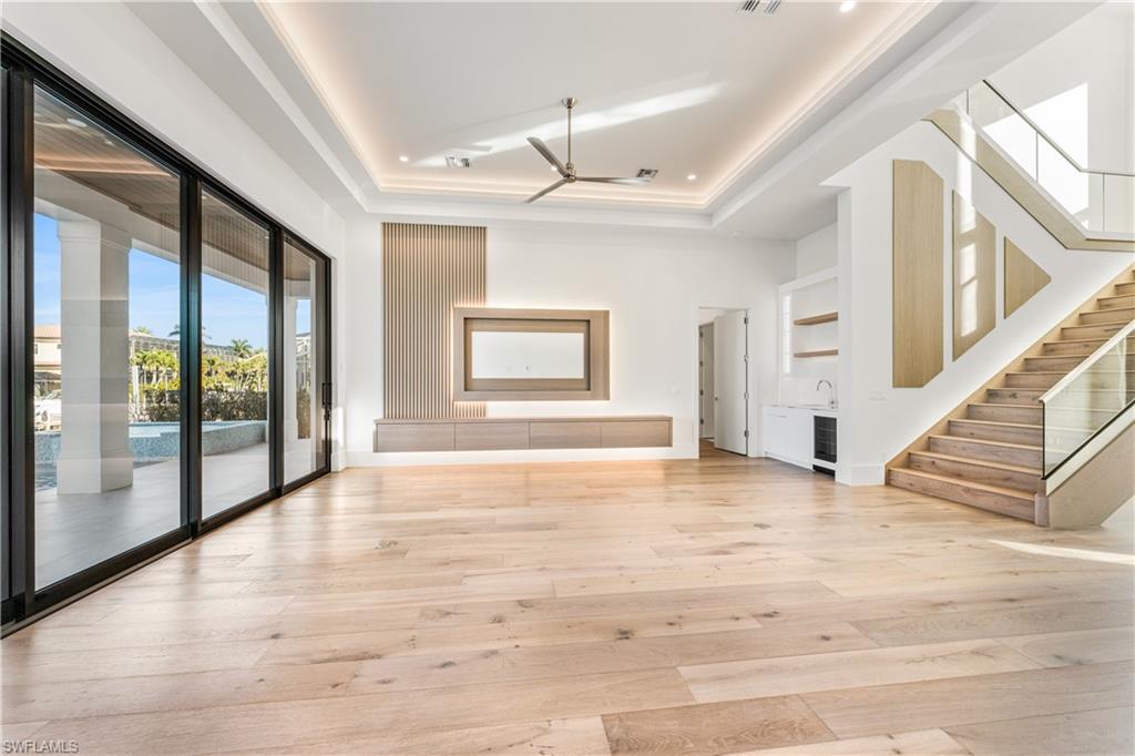 Unfurnished living room with light wood-type flooring, a tray ceiling, a ceiling fan, and beverage cooler