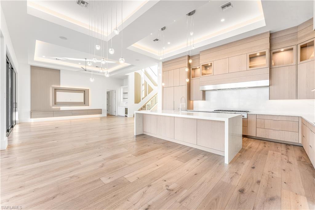 Kitchen with glass insert cabinets, a tray ceiling, light wood finish cabinetry, modern cabinets, and decorative light fixtures