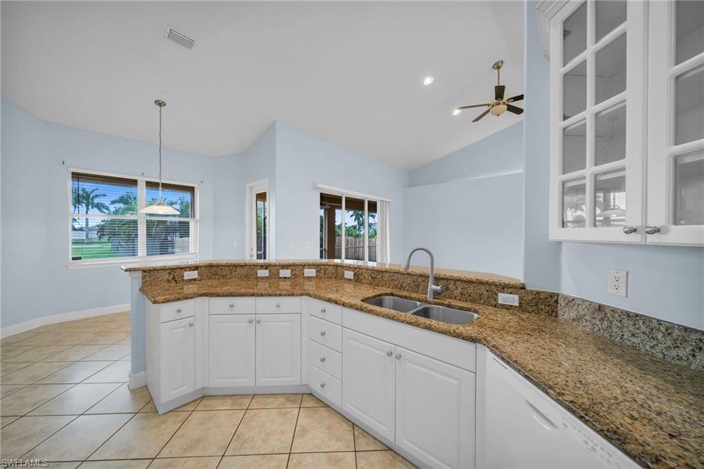 Kitchen with white cabinets, dark stone countertops, hanging light fixtures, light tile patterned floors, and vaulted ceiling
