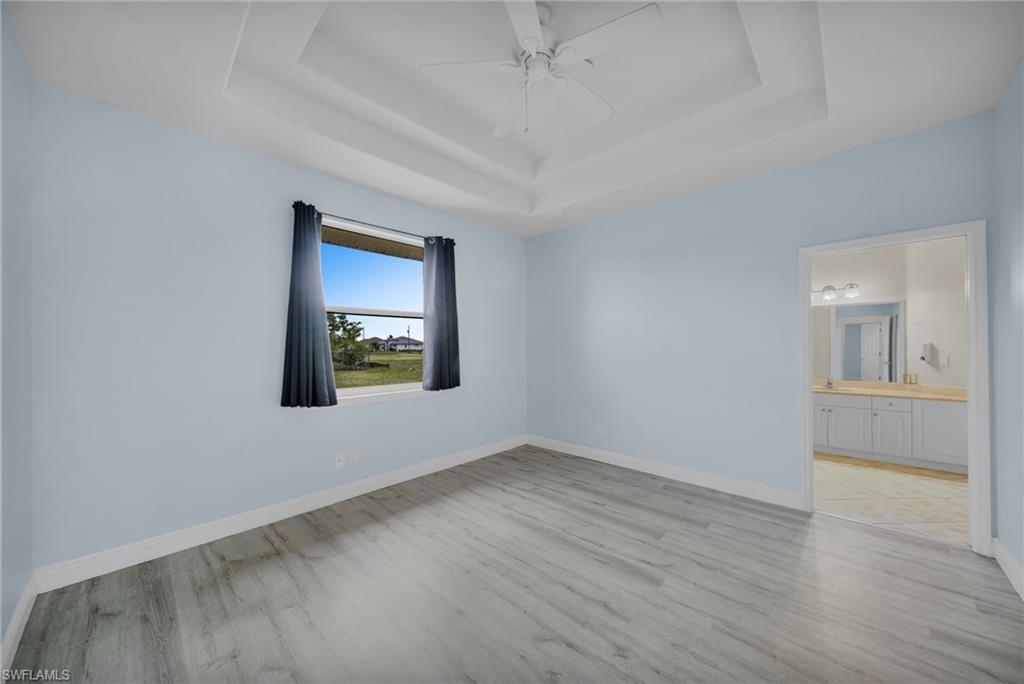 Unfurnished bedroom with a tray ceiling, a ceiling fan, light wood-type flooring, and connected bathroom