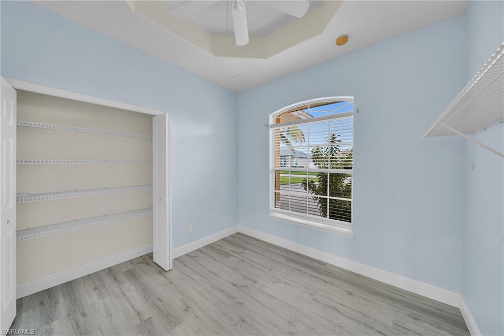 Unfurnished bedroom with a raised ceiling, a closet, light wood-style floors, and a ceiling fan