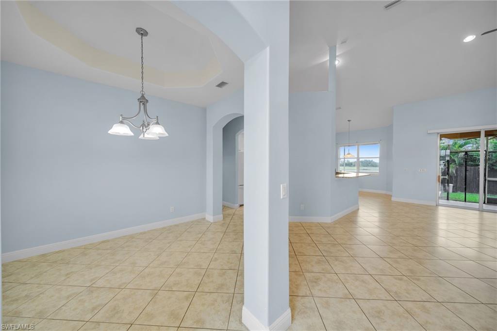 Unfurnished room with a chandelier, light tile patterned flooring, arched walkways, and a tray ceiling