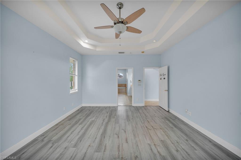 Unfurnished bedroom with light wood finished floors, a ceiling fan, ensuite bath, and a tray ceiling
