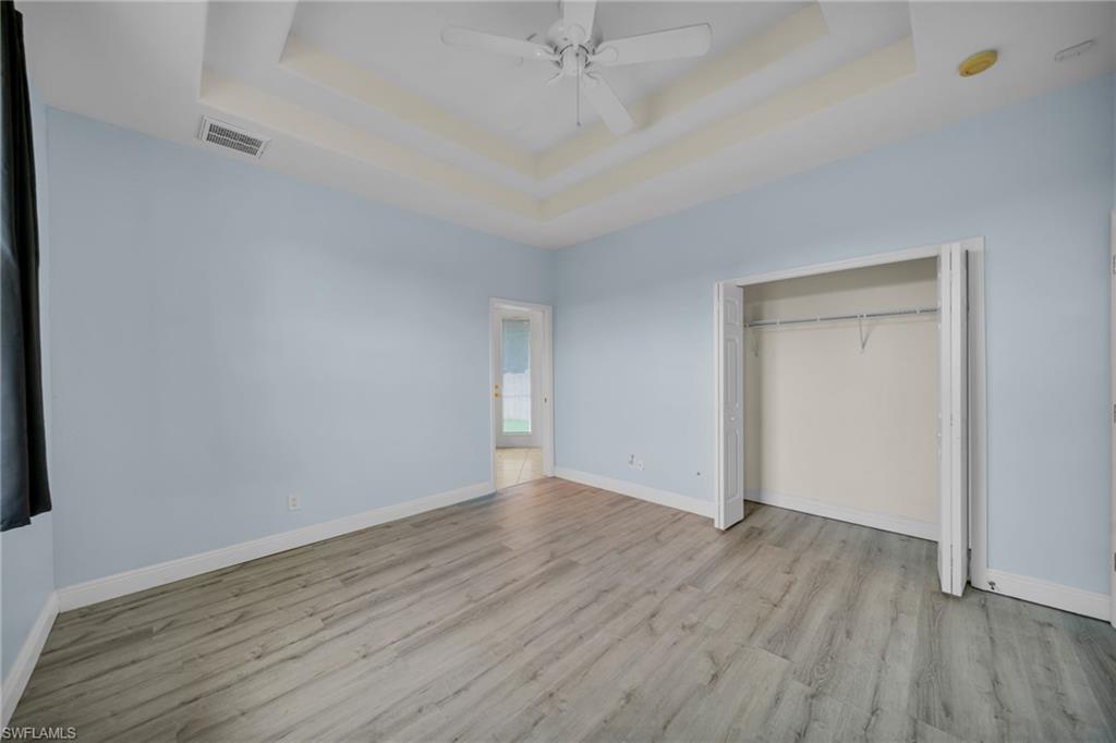 Unfurnished bedroom with light wood finished floors, a tray ceiling, a ceiling fan, and a closet