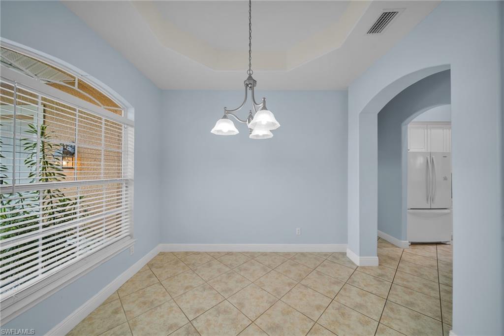 Unfurnished room with arched walkways, light tile patterned floors, a raised ceiling, and a chandelier