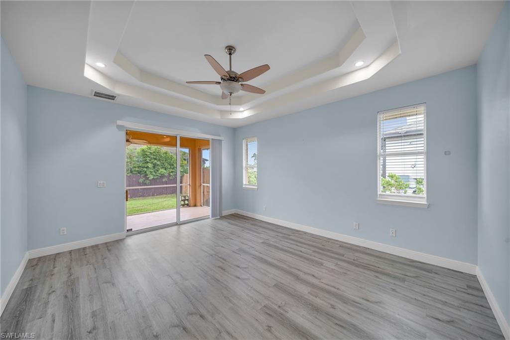 Unfurnished room with light wood finished floors, ceiling fan, and a tray ceiling