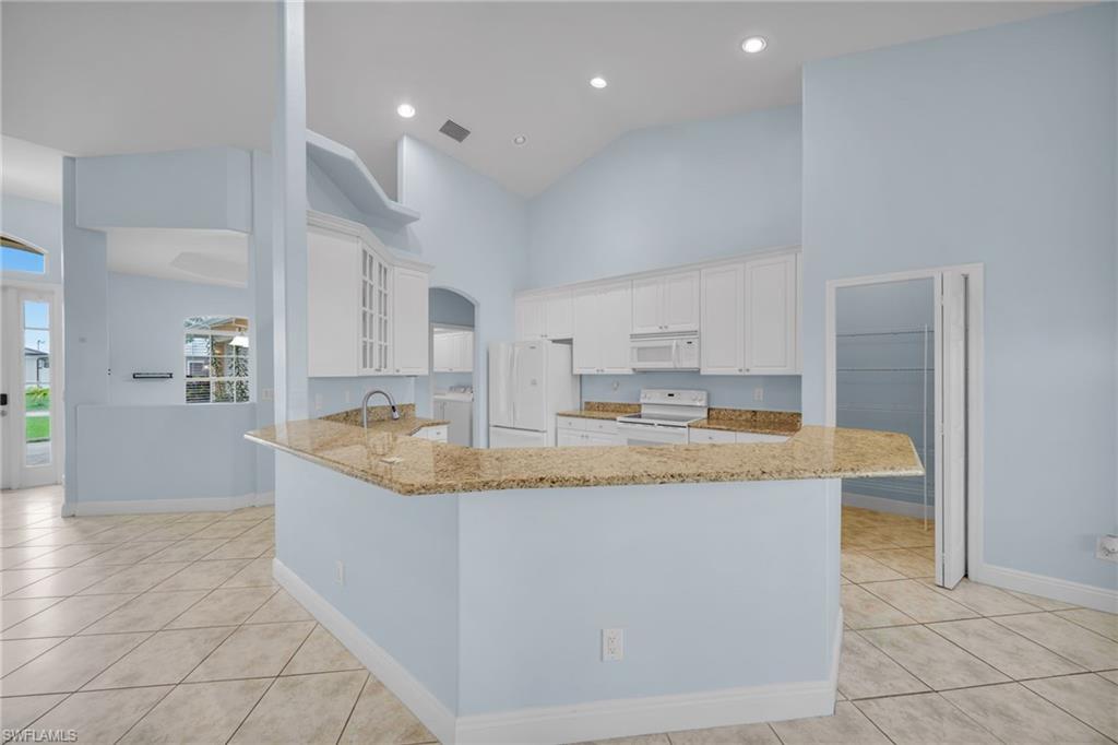 Kitchen featuring high vaulted ceiling, white cabinetry, white appliances, light stone countertops, and glass insert cabinets