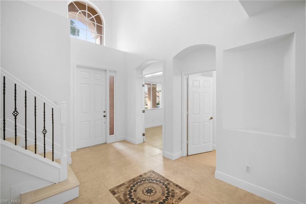 Foyer with arched walkways, a towering ceiling, light tile patterned flooring, and stairway