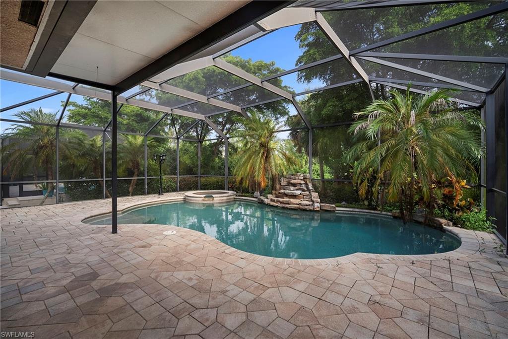 View of pool featuring glass enclosure, a pool with connected hot tub, a sunroom, and a patio area