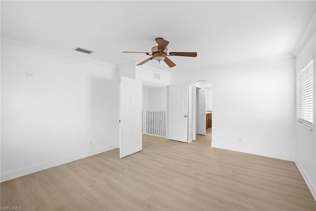 Bedroom featuring crown molding, light wood-type flooring, arched walkways, and ceiling fan