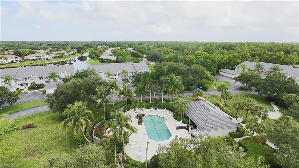 Outdoor swimming pool with a surrounding paved deck, adjacent clubhouse with a tile roof, and mature palm trees