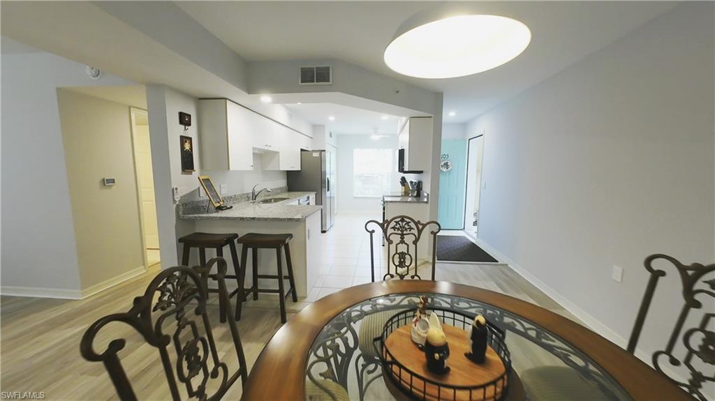 Kitchen and dining area featuring light wood-finish flooring, white cabinetry, stainless steel appliances, and a breakfast bar with stone countertops