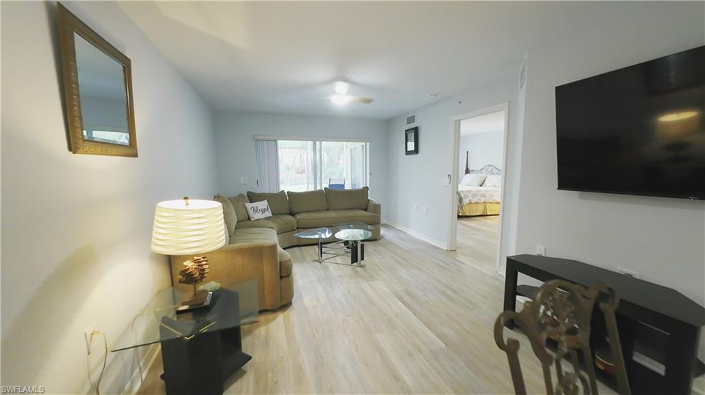 Bright and open living area showcasing wood-finish flooring throughout, a comfortable seating arrangement, and abundant natural light from multiple windows