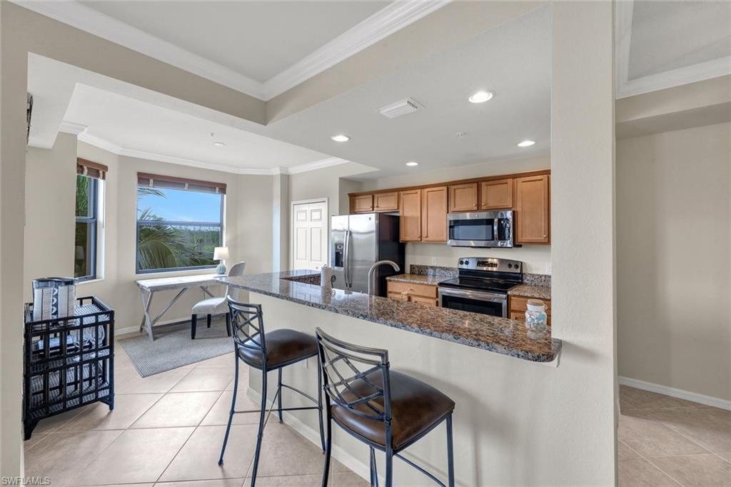 Kitchen featuring a kitchen bar, crown molding, dark stone countertops, appliances with stainless steel finishes, and light tile patterned floors