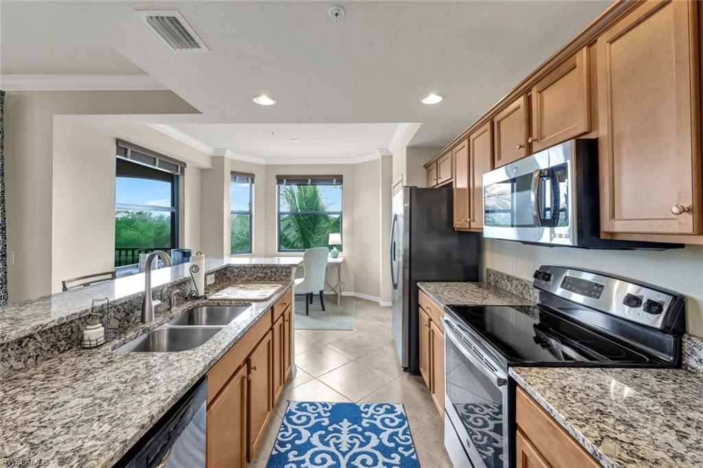 Kitchen featuring stainless steel appliances, crown molding, light stone counters, light tile patterned floors, and brown cabinetry