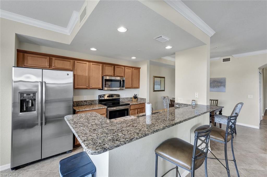 Kitchen with crown molding, a kitchen breakfast bar, stainless steel appliances, brown cabinetry, and dark stone counters
