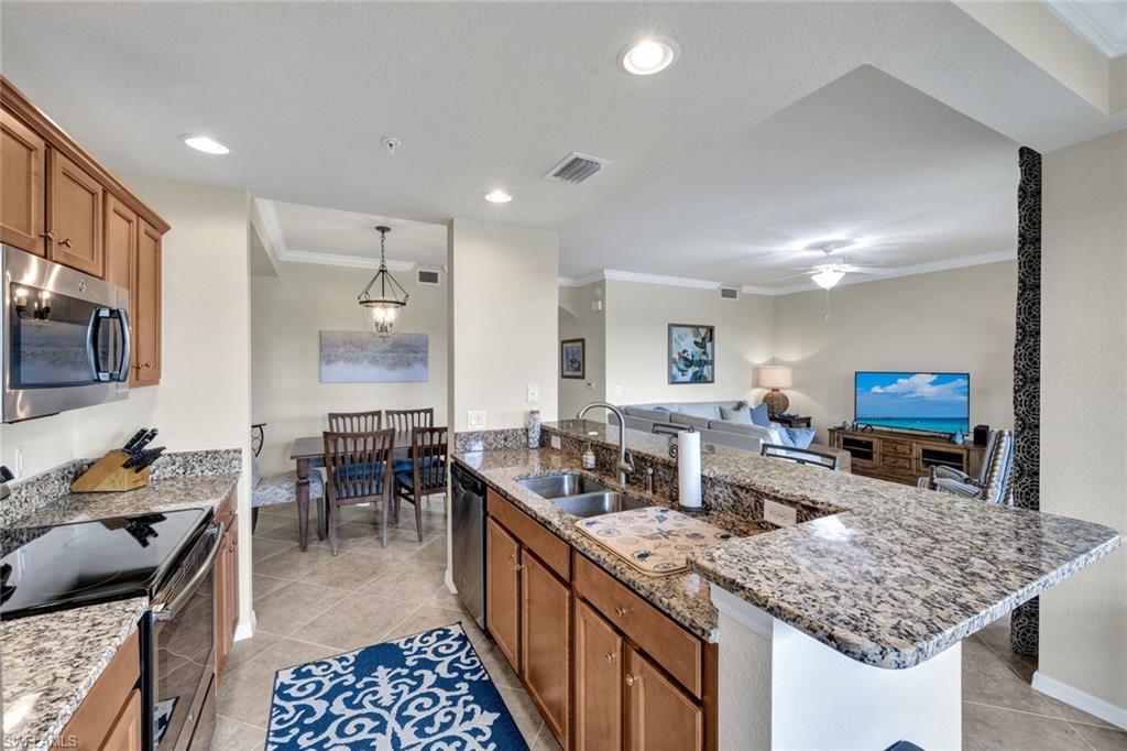 Kitchen with crown molding, brown cabinets, appliances with stainless steel finishes, light stone countertops, and light tile patterned flooring