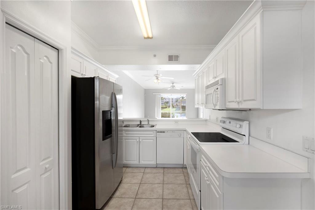 Kitchen with white appliances, white cabinets, light tile patterned flooring, light countertops, and crown molding