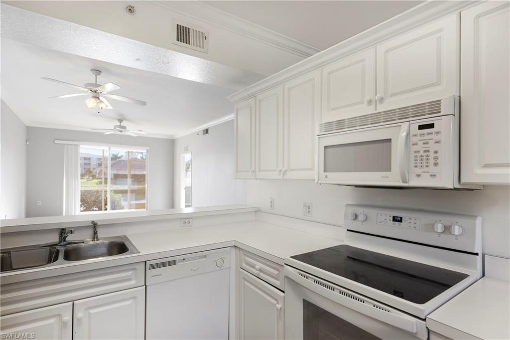 Kitchen featuring white appliances, white cabinetry, ornamental molding, light countertops, and ceiling fan