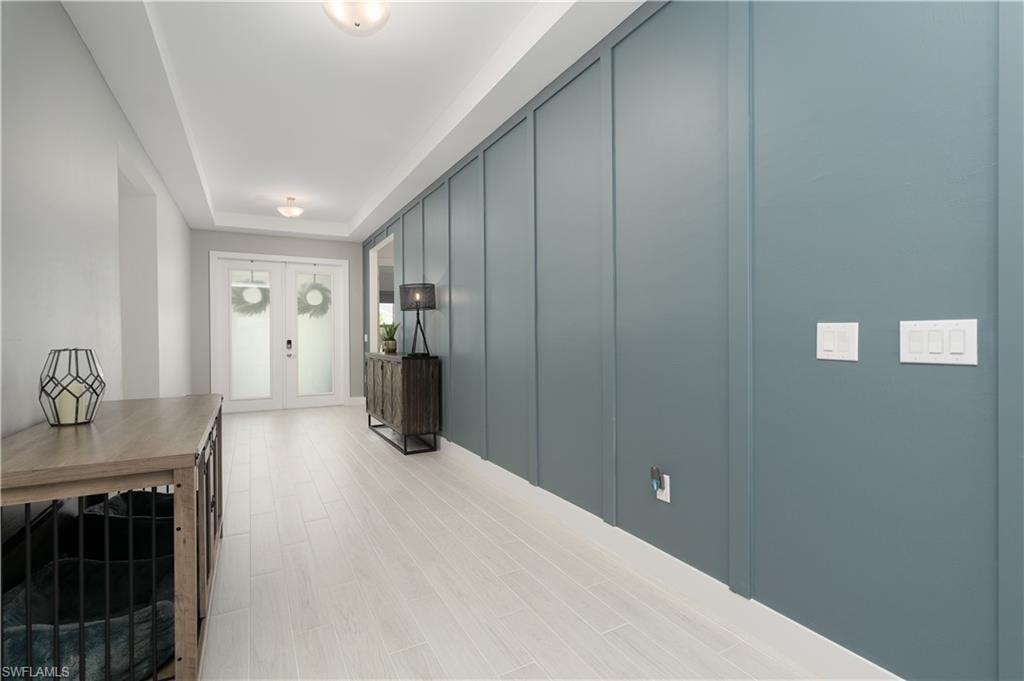 Hall with wood finished floors, a tray ceiling, and french doors