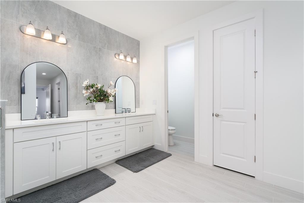 Bathroom featuring double vanity, tile walls, and light wood-style floors